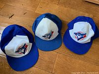 Three vintage Toronto Blue Jays baseball snapback caps laying on wood floor, front side visible with logo.