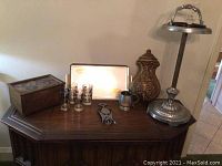 Full view of vintage barware items on wooden surface including tall metal ashtray stand, drinking glasses, metal tray, bottle opener, creamer, and wooden chest.