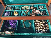 Top layer of jewelry box showing earrings, brooches, and small jewelry items organized into compartments with green velvet lining.