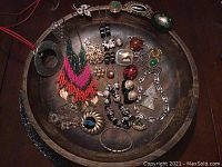 Top view of all jewelry pieces displayed in a round wooden bowl, showing variety of necklaces, bracelets, earrings, rings, and brooches.