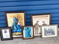 Group photo showing all five framed art pieces arranged on a floor against a blue door, showcasing variety in size and subject matter.