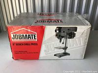 Original box displaying Jobmate 8-inch bench drill press with product image and specifications including 2.4A induction motor and speeds of 620, 1100, 1720, 2340, and 3100 RPM.