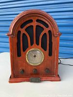 Front view of vintage wood cathedral style Elgin radio showing arched top, black speaker areas, circular dial and wood housing with metal nameplate.