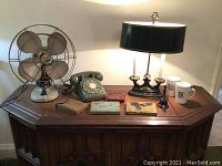 Photo showing the full lot displayed on a wooden corner table, including the fan, rotary phone, lamps, mugs, and collectible tins.