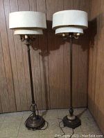 Full view of the two retro brass floor lamps standing side by side, showing double fabric shades and aged brass finish.