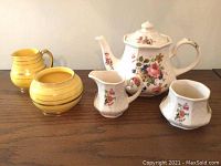 Front view of the Sadler floral tea set including teapot, creamer, sugar bowl, and two yellow ceramic pots on a wooden surface.