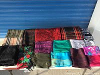 Top view of 15 folded scarves laid out on a white surface in multiple rows showing patterns and colors.