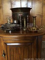 Full view of the solid brass bucket, candlesticks, silver-toned bowls, and other items on wooden cabinet