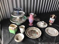 Full view of all ceramic items arranged on black cloth, showing various plates, vases, a tiered cake stand, pitcher, and cups