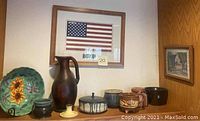 Framed American flag commemorating 9-11, tall brown pottery vase, variety of small art pottery bowls and vases, and framed watercolor painting on wall