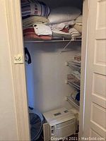 Closet with folded bed sheets, towels, white portable floor fan, and Maytag air conditioner on floor