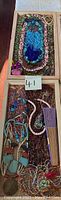 Wide shot showing multiple beaded necklaces, belts, and a folding hand fan arranged in a wooden box.