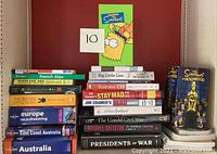 Photo showing multiple books stacked vertically including titles on travel, technology and history, topped with The Simpsons VHS tapes box set
