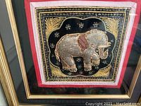 Framed artwork showing Burmese Kalaga embroidery with an elephant in gold thread on black velvet and red trim.