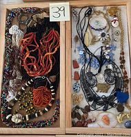 Full view of costume jewelry in two wooden trays including multiple beaded necklaces, belts, brooches, and pendants.