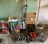 Full view of garden supplies including various bags of fertilizer, potting mix, ice melter, gardening hand tools, small chain saw, baskets, and wooden crate