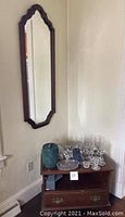 Wall mirror mounted on wall above wooden end table holding glassware and decorative items
