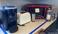 Photo showing Keurig coffee maker, Sunbeam toaster, microwave oven, stainless steel travel mug, French press, and toast rack on kitchen counter.