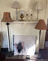 Full view of two floor lamps, metal winged frog planter, vintage sad iron, and tabletop lamps on mantle