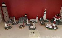 Overview of twelve miniature chalkware lighthouses arranged on shelf, showing size variation and different base types