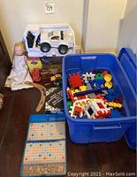 Overview of miscellaneous toys including white remote-control pickup truck, doll, blue container with building blocks, wooden boomerang, and small toy vehicle on floor
