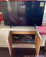 Philips flatscreen TV on top of a white cabinet with open doors showing DVDs, VHS tapes, and a Sony DVD player inside the cabinet.