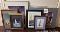 A collection of seven framed prints and artworks featuring lighthouses and buildings in various wood and metal frames.