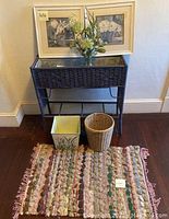 Full view of lot showing two framed floral prints on wall, dark brown wicker planter table, ceramic planter, wicker basket, and multicolored woven scatter rug on hardwood floor.