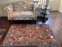 Full view of floral upholstered sofa, floral rug, and pie crust tilt top table near window