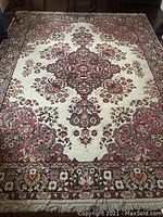 Full view of rug showing ivory field, central burgundy medallion, floral border and fringe on one end