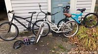 Overview of three women's bicycles leaning against a house wall, along with helmets and locks on the ground in front.