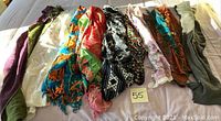 Photo showing 9 multicolored women's scarves laid out on a bed including various patterns and colors, some with fringes.