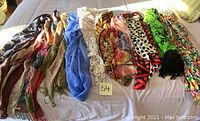 Multiple women's scarves with various vibrant patterns and colors displayed on a bed.