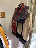 Two images showing purple woven tote bag and red leather crossbody bag hanging alongside fabric clothing items