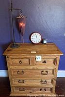 Photo of wooden chest with four drawers, lamp, and two clocks on top against a purple wall