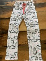 Full view of the fuzzy pajama pants laid flat on a wooden floor, showing unicorn print and coral pink drawstring.