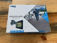 Front of sealed retail box showing Lorex FLIR branding, image of two cameras and 7" monitor.