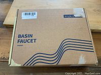 Closed box labeled 'Basin Faucet' with simple graphics on corrugated cardboard