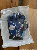 Blue and black pet grooming gloves shown in sealed clear packaging on a wooden floor.