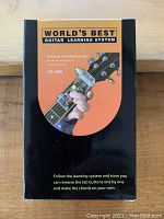 Front of box for World's Best Guitar Learning System KG-386 showing colored button device illustration on guitar neck and learning instructions.