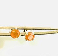 Close-up front view of round faceted orange carnelian stones in sterling silver prong settings held by tweezers.