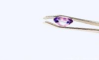 Individual purple amethyst gemstone held with tweezers showing clarity and cut