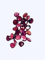 25 natural rhodolite garnet gemstones of mixed shapes and deep red/purple/pink hues laid out on a white background.