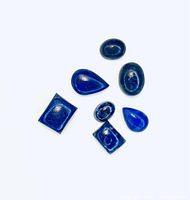 Seven deep blue lapis lazuli cabochons in various shapes arranged on a white background.