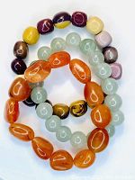 Three gemstone bracelets shown intertwined: orange carnelian, green aventurine, and multicolored mookaite jasper beads on elastic cords.