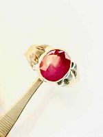 Top view of oval faceted pinkish-red ruby in bezel setting, silver band visible
