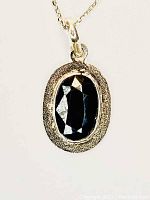 Close-up of pendant showing oval blue sapphire and textured silver bezel