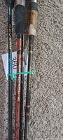 Photo showing three fishing rods laid side by side on carpet, identifiable brands include Abu Garcia Black Max and Shakespeare Ugly Stik Original Z, plus a third rod possibly Cardinal.