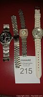 Four watches and parts displayed on red surface with MaxSold auction tag