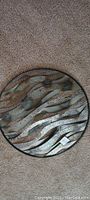 Top-down photo of round metal wall art on carpeted floor showing the textured wavy metal strips design within circular metal frame.